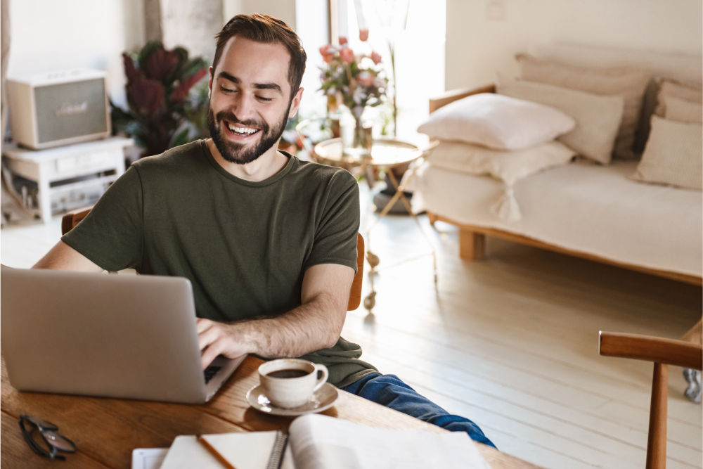 Remote worker smiling while using a laptop at home, illustrating the importance of secure remote work data disposal in a hybrid work environment.